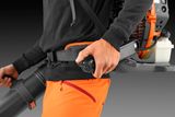 A person operating a backpack leaf blower, focusing on the handle and control grip.