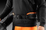 Person holding a leaf blower with hip belt, wearing work gear.