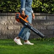A person using a leaf blower to clear fallen leaves in a garden.