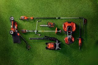 Top view of various gardening tools arranged on grass, including a lawn mower, hedge trimmer, and leaf blower.