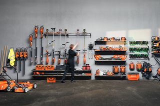 Eine Person, die eine Vielzahl von Husqvarna Garten- und Bauwerkzeugen auf einem Wand-Display organisiert.