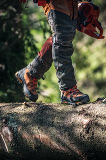 A person walking on a large tree trunk, showcasing work boots and a chainsaw.
