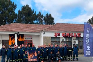 Ομάδα εργαζομένων με μπλε εξοπλισμό εργασίας ποζάρουν με εξοπλισμό μπροστά από ένα κτίριο.