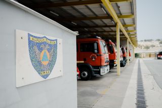 Μια σειρά από πυροσβεστικά οχήματα σταθμευμένα σε έναν πυροσβεστικό σταθμό με μια πινακίδα που εμφανίζει ένα έμβλημα ασπίδας.
