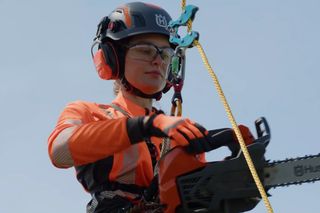 En person i arbetskläder som använder en motorsåg från Husqvarna medan han är upphängd i ett rep.