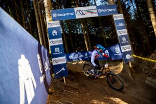 Un ciclista che percorre una discesa sotto un arco con marchio Husqvarna in un ambiente boschivo.