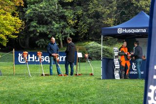 Persone che interagiscono con i prodotti Husqvarna durante un evento all'aperto, con striscioni e una tenda visibili.