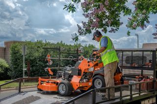 A person in work gear operating a ride-on mower on a trailer.