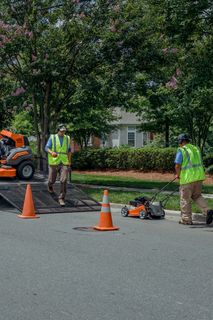 Workers unloading lawn mowers from a truck in a residential area.