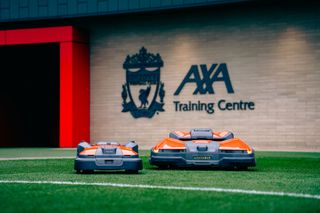 Two robotic lawn mowers on a grass field in front of a training center.