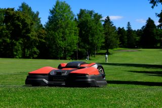 遠くに 2 人がいるゴルフコースのフェアウェイ上のロボット芝刈機。