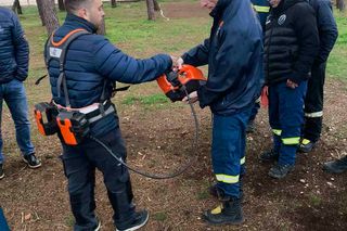 Ομάδα εργατών σε δασικό περιβάλλον, εξετάζοντας ένα εργαλείο κατασκευής.