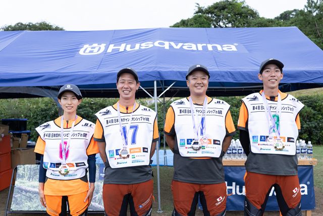 屋外イベントで番号の付いたベストを着てハスクバーナのテントの下に立っている4人の参加者。