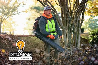 A person using a leaf blower to clear fallen leaves in a park setting, with a PTIA 2025 Award Winner badge visible.