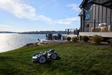 A robotic lawn mower operating on a well-maintained lawn in front of a lakeside home with a HGTV Dream Home 2026 logo overlay.