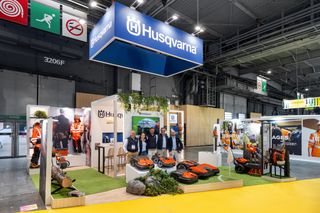 Stand d’exposition Husqvarna avec des robots tondeuses et des outils électriques, avec le personnel et des mannequins.