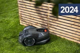Robotgräsklippare som arbetar bredvid ett trästaket med ett överlägg från 2024.