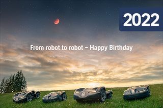 Fyra robotgräsklippare på ett gräsbevuxet fält under en solnedgångshimmel med en måne.