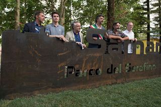 Gruppo di persone in piedi dietro un grande cartello metallico in un parco.