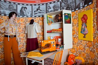 Vintage-Nähzimmer-Einrichtung mit orangefarbener Nähmaschine, Schaufensterpuppen und Retro-Dekor.