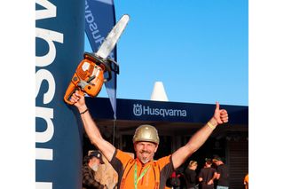 Eine Person mit einer Husqvarna-Motorsäge, die bei einer Veranstaltung im Freien den Daumen nach oben streckt.