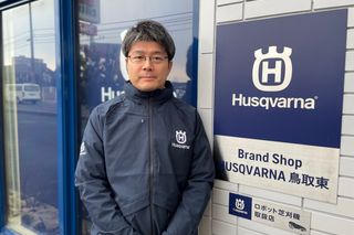 ハスクバーナブランドの店の外で、店名が書かれた看板の横に立っている人。