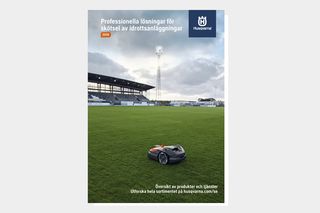 En robotgräsklippare som arbetar på en idrottsplats med stadionsittplatser i bakgrunden.