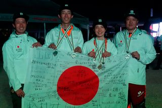 夜間イベントでメダルと署名入りの日本国旗を持つ4人の個人。