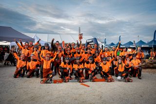 Grupp av människor i arbetsutrustning som poserar med motorsågar vid en utomhushändelse.