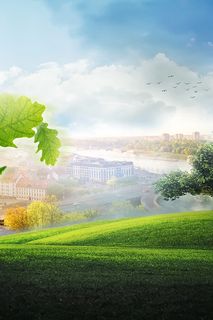 Malebný pohľad na mesto s kostolom, mostom a stromom na trávnatom kopci pod modrou oblohou.