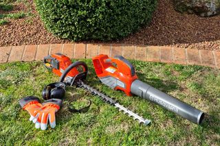 A Husqvarna hedge trimmer and chainsaw placed on grass with gloves and ear protection.