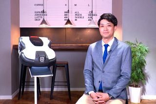屋内に展示されているハスクバーナのロボット芝刈り機の隣に座っている人物。
