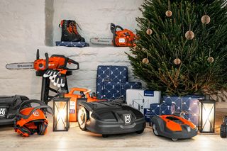 Eine festliche Ausstellung von Husqvarna Garten- und Outdoor-Produkten, darunter Mähroboter, Motorsägen und Arbeitsausrüstung, arrangiert um einen geschmückten Weihnachtsbaum mit Geschenkboxen und Laternen.