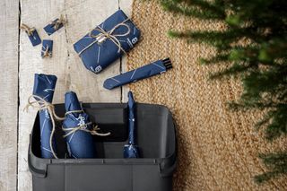 Husqvarna Geschenkartikel in blauem Papier mit Bindfaden in einem schwarzen Behälter auf Holzboden verpackt.