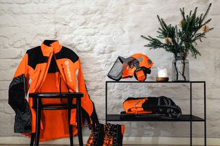 Eine Reihe von Husqvarna Arbeitskleidung, einschließlich einer Jacke, Stiefeln und Helm, die auf einem Stuhl und einem Regal ausgestellt sind.