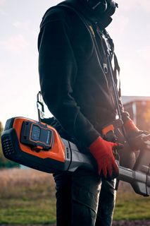 Osoba, ktorá drží produkt Husqvarna na poli počas západu slnka.