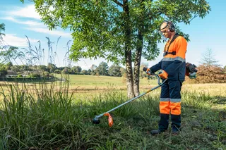 A person using a grass trimmer to cut tall grass in a field.