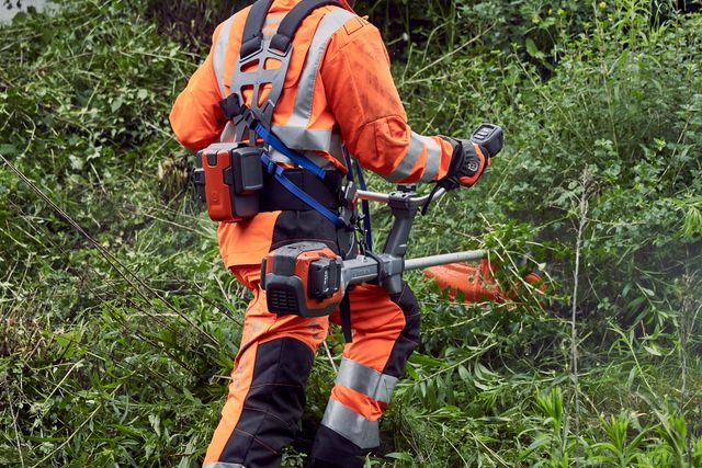 En person som använder en buskröjare för att trimma tät vegetation i en sluttning.