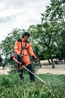Eine Person, die einen Rasentrimmer in einem Park mit einem Seilbahnturm im Hintergrund verwendet.