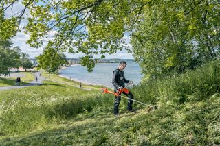 Een persoon die een grastrimmer gebruikt om gras te maaien op een helling bij een meer.