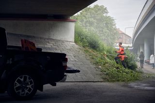 Een persoon die een trimmer gebruikt om gras te maaien op een helling onder een brug.