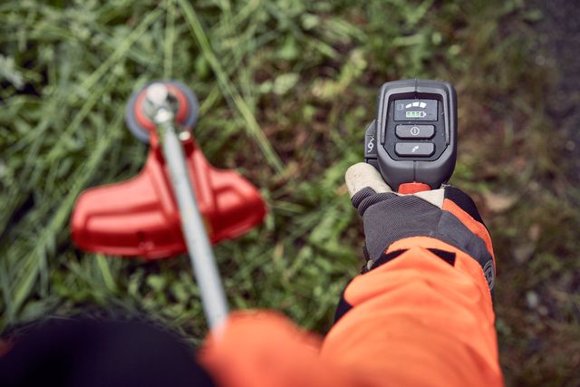 A person holding a grass trimmer, focusing on the control panel, with grass in the background.
