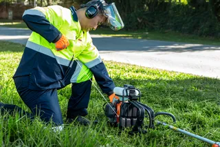 A person in work gear using a core drill on a grassy area.