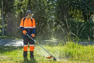 A person using a grass trimmer to cut tall grass in a garden setting.