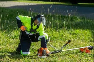 Máy cắt cỏ HUSQVARNA 541RS. A person using a grass trimmer on a grassy area.
