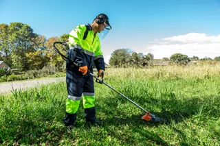 A person using a grass trimmer to cut grass in a sunny outdoor setting.