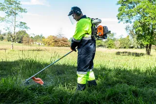 A person using a brushcutter to trim grass in a grassy field.