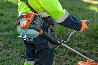 A person using a grass trimmer in a garden setting.