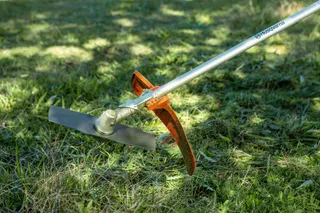 A gardening tool with a long handle lying on grass.