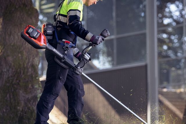 En person som använder en trådtrimmer för att klippa gräs nära ett träd.